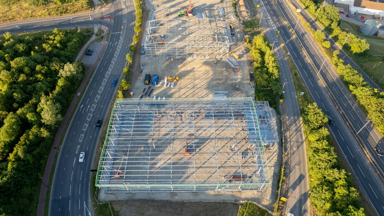 Aerial view of a large steel-framed building going up beside a road