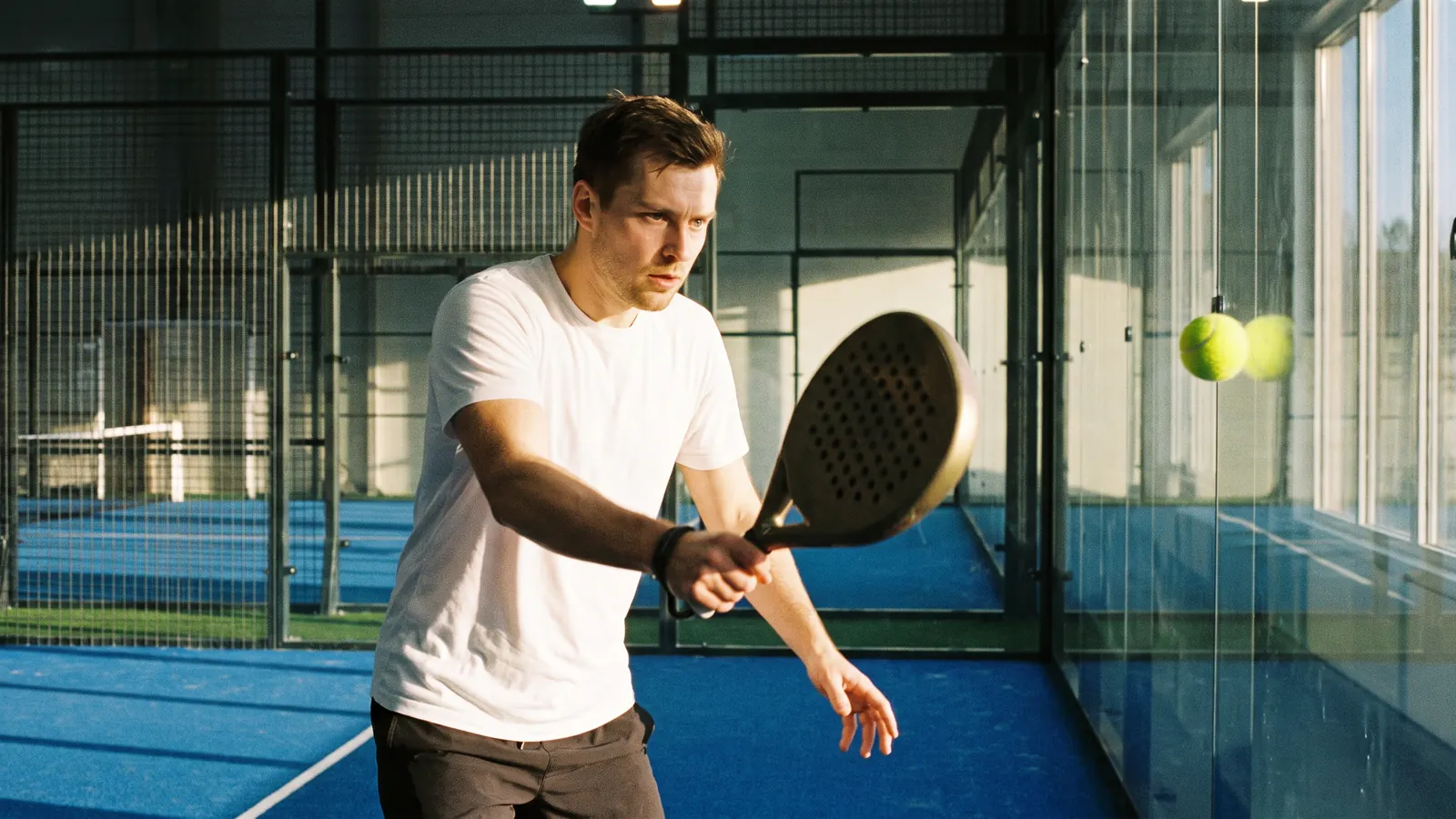 A player hitting a backhand off the glass wall on an indoor court