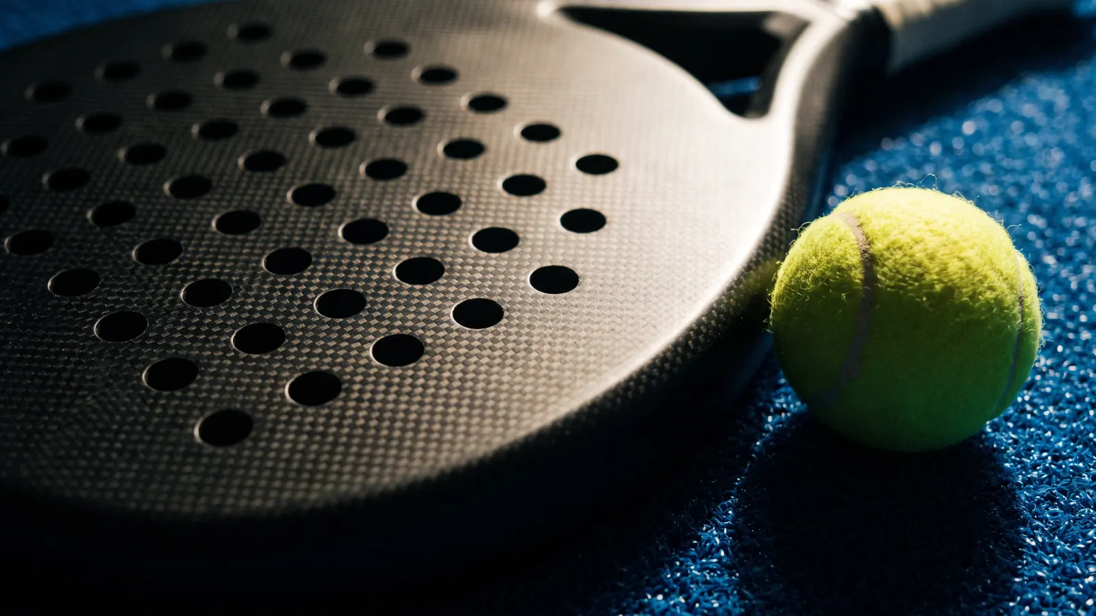 Close-up of a perforated carbon padel racket and ball